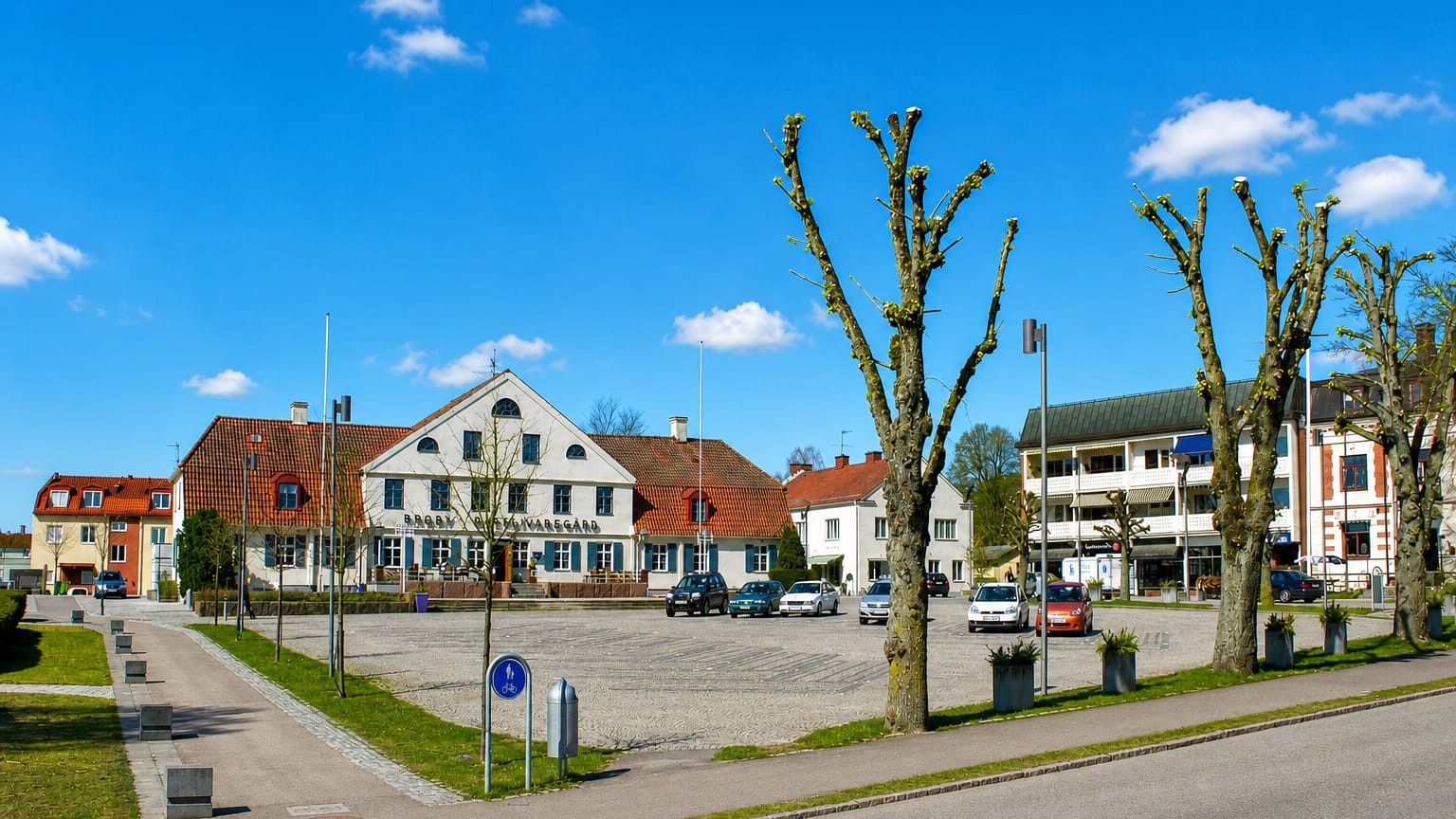Market square in Broby, Skåne, with a white gabled building, pollarded trees and cobbled paving
