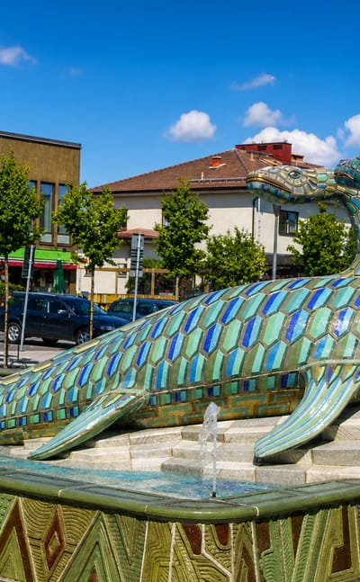 The tiled ceramic fish fountain sculpture on a square in Bromolla with town buildings behind