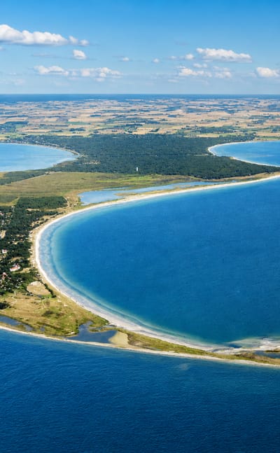 Aerial view of the sandy Falsterbo peninsula and lighthouse curving into the blue Baltic Sea, Sweden