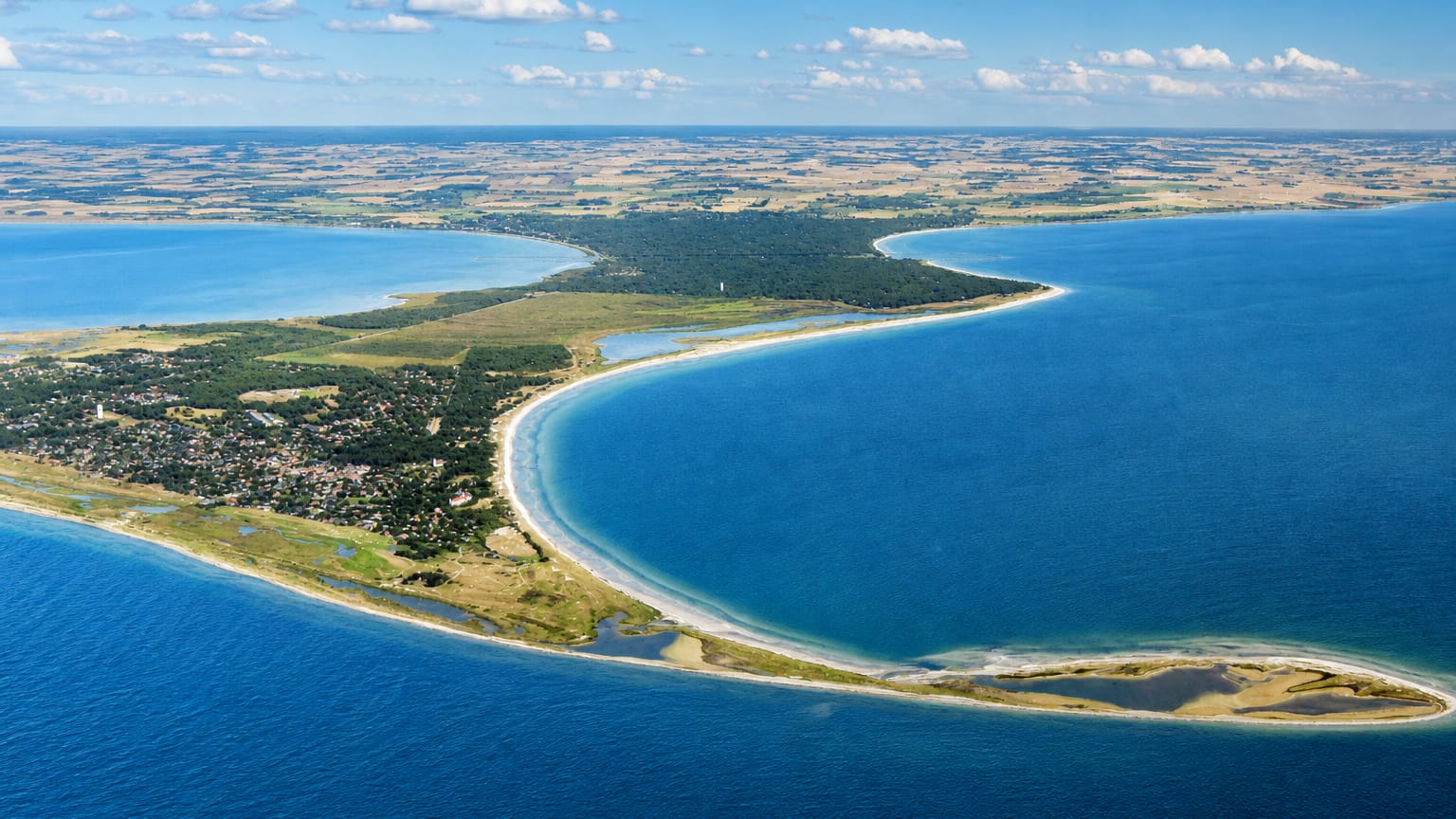 Aerial view of the sandy Falsterbo peninsula and lighthouse curving into the blue Baltic Sea, Sweden
