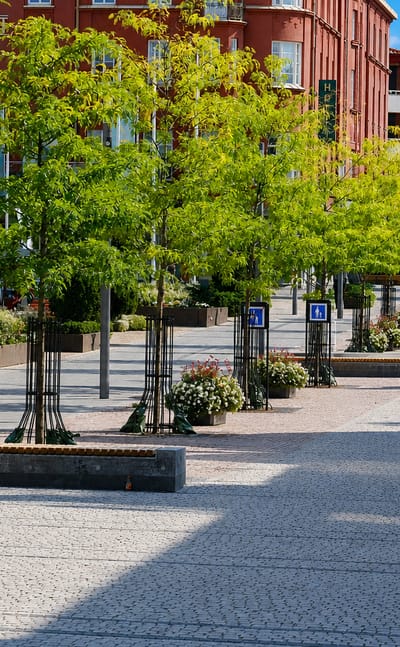 Tree-lined pedestrian square with red-brick buildings and a church spire in Hassleholm, Sweden.