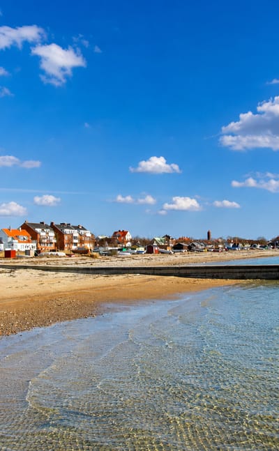 Sandy beach and shallow Öresund water fronting the colourful waterfront houses and harbour pier of Råå, Sweden.