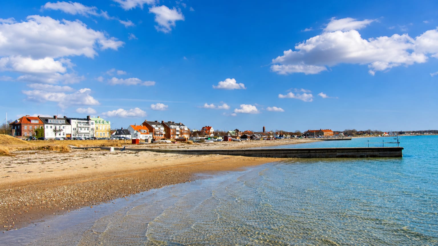 Sandy beach and shallow Öresund water fronting the colourful waterfront houses and harbour pier of Råå, Sweden.