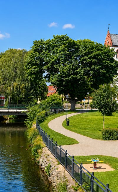 Whitewashed Hörby church tower above a riverside park with footpaths, lawns and apartment buildings, Sweden.