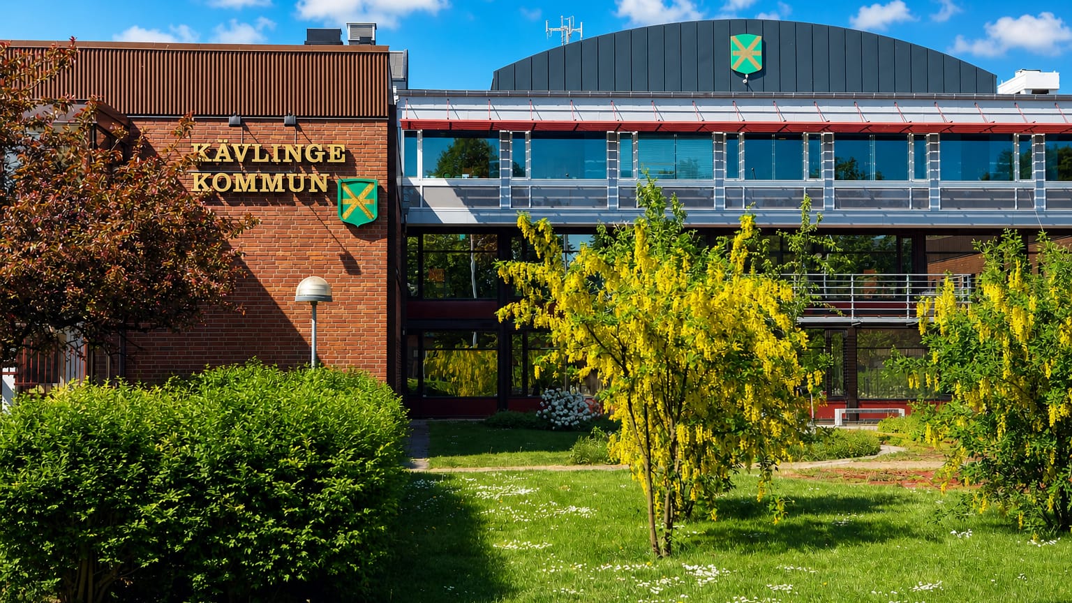 The red-brick Kavlinge Kommun municipal building with its crest and a landscaped garden in Kavlinge, Sweden.
