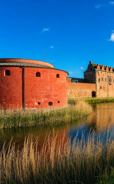 Malmöhus Castle's round red-brick gun tower reflected in its moat under a bright blue sky in Gamla Staden, Malmö, Sweden