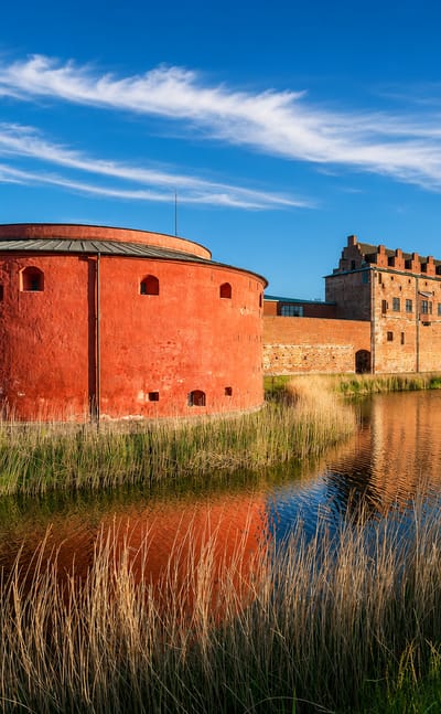 Malmöhus Castle's red round bastion reflected in its moat with reeds, Slottsstaden, Malmö, Sweden