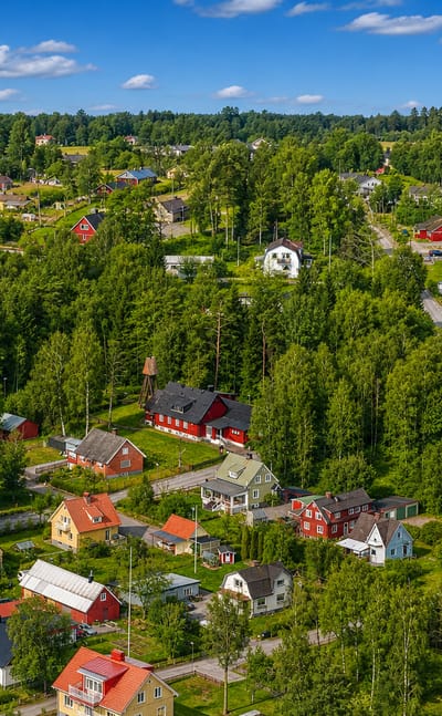 Aerial view over the scattered red and coloured houses of Orkelljunga amid dense green forest, Sweden.