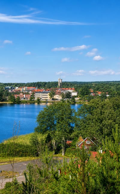 Lakeside view of Osby, Sweden, showing its water tower and church across the blue lake framed by birch trees.