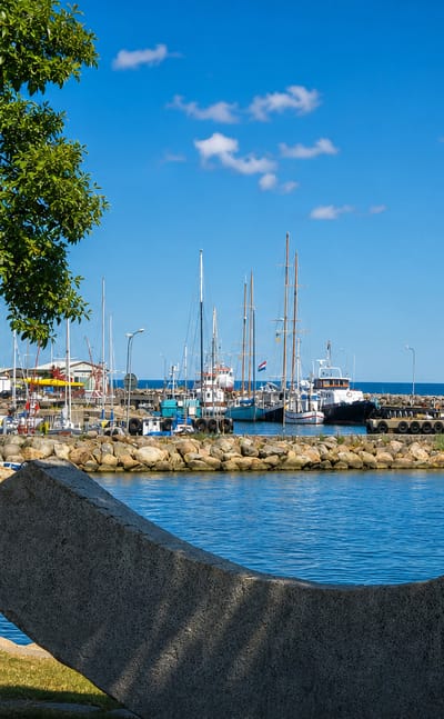 Simrishamn harbour, Sweden, with moored sailing boats, flags and a stone sculpture beside the calm blue water
