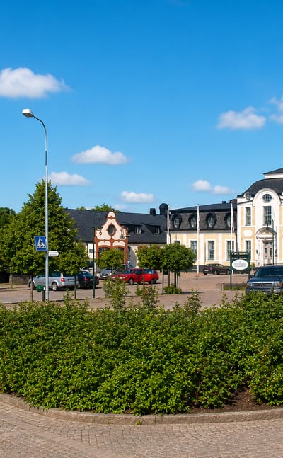 Sjobo town square with a grand cream manor building, clock facade, benches and clipped hedges in summer.