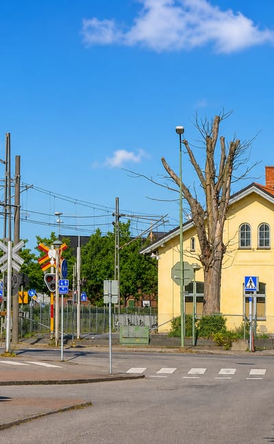 Sunny street scene in Skurup with a yellow railway station building, a level crossing and clear blue sky.