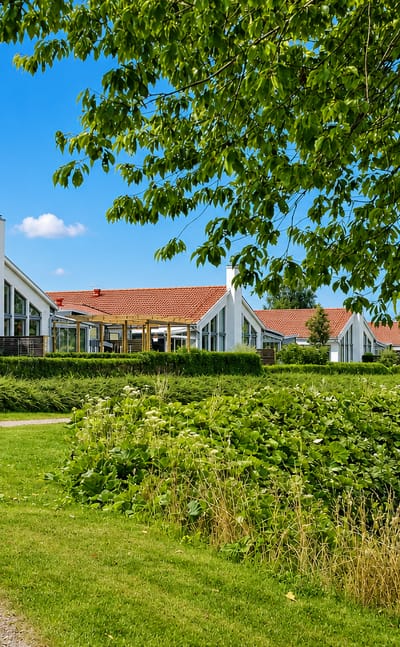 Modern white gabled houses with red-tiled roofs behind a hedge and gravel path in Svalöv, Sweden.