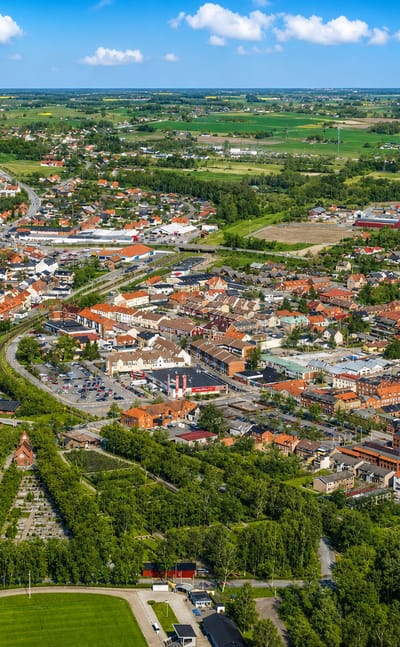 Aerial view of Tomelilla, Sweden, its red-roofed town centre ringed by fields and farmland under a blue sky