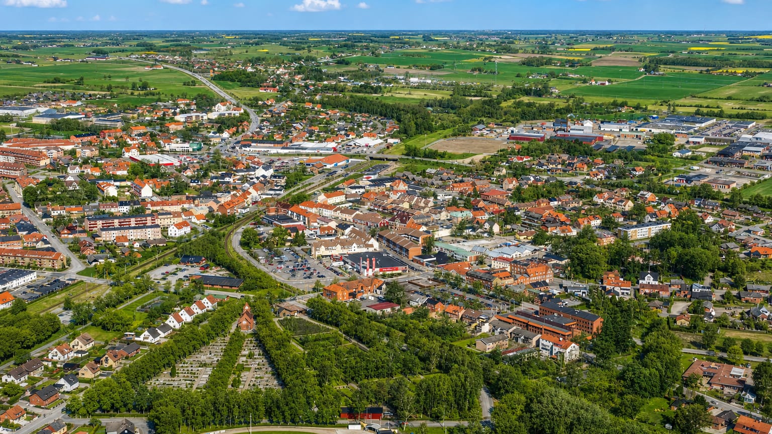 Aerial view of Tomelilla, Sweden, its red-roofed town centre ringed by fields and farmland under a blue sky