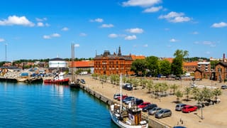 Ystad harbour, Sweden, with moored boats, a red-brick landmark building and the quayside under a bright blue sky.