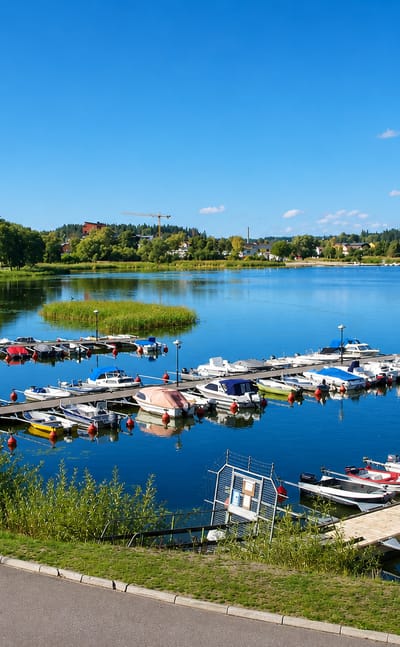 Small-boat marina with pontoons on the calm lake at Gnesta, Sweden, the town rising beyond on a clear summer day.
