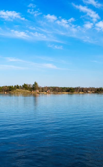 Wooden jetty and forested archipelago islands under a blue sky at coastal Oxelosund, Sweden.