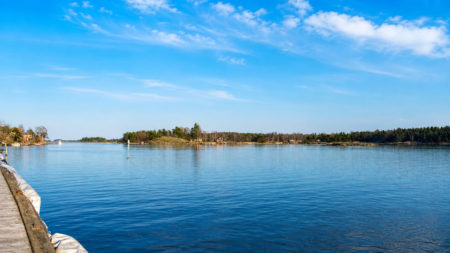 Wooden jetty and forested archipelago islands under a blue sky at coastal Oxelosund, Sweden.