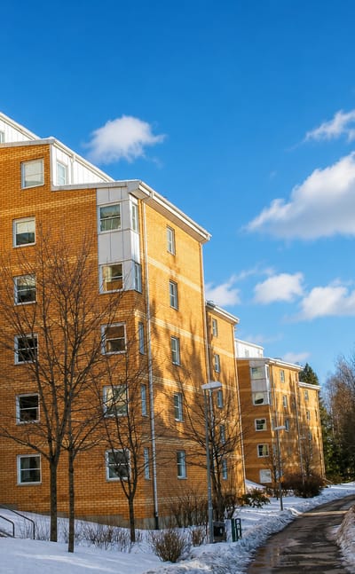Yellow-brick apartment blocks with balconies among bare trees and snow in Bollmora suburb, Sweden