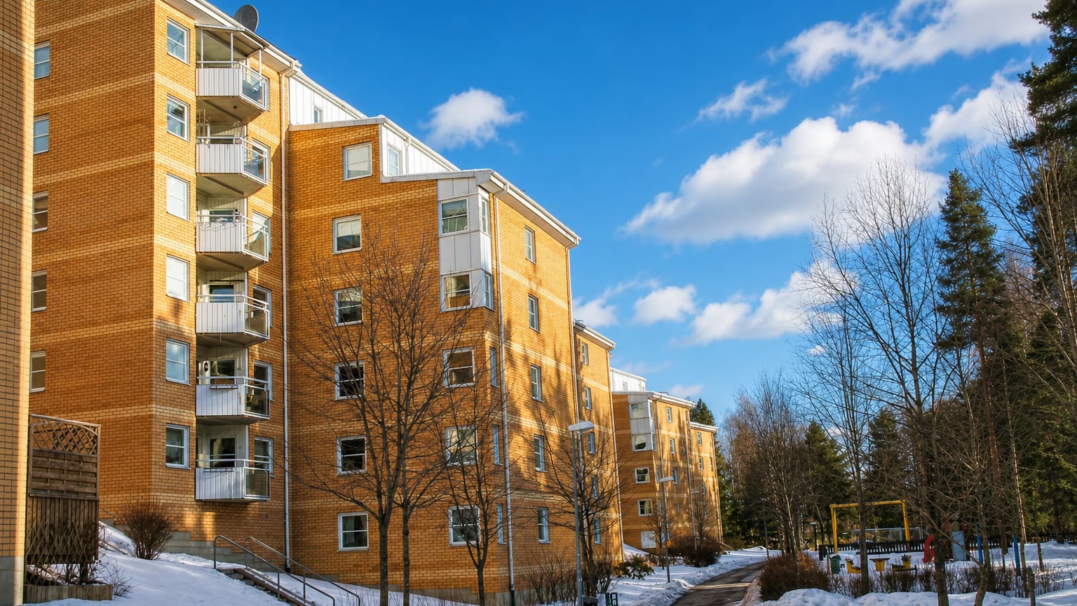 Yellow-brick apartment blocks with balconies among bare trees and snow in Bollmora suburb, Sweden