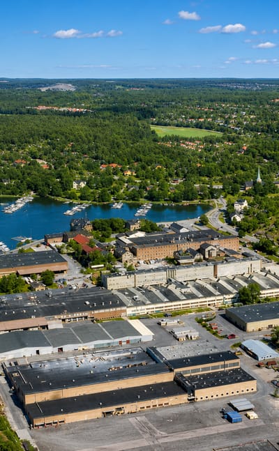 Aerial view of Gustavsberg's lakeside porcelain factory complex, marina and archipelago woodland under a blue summer sky.