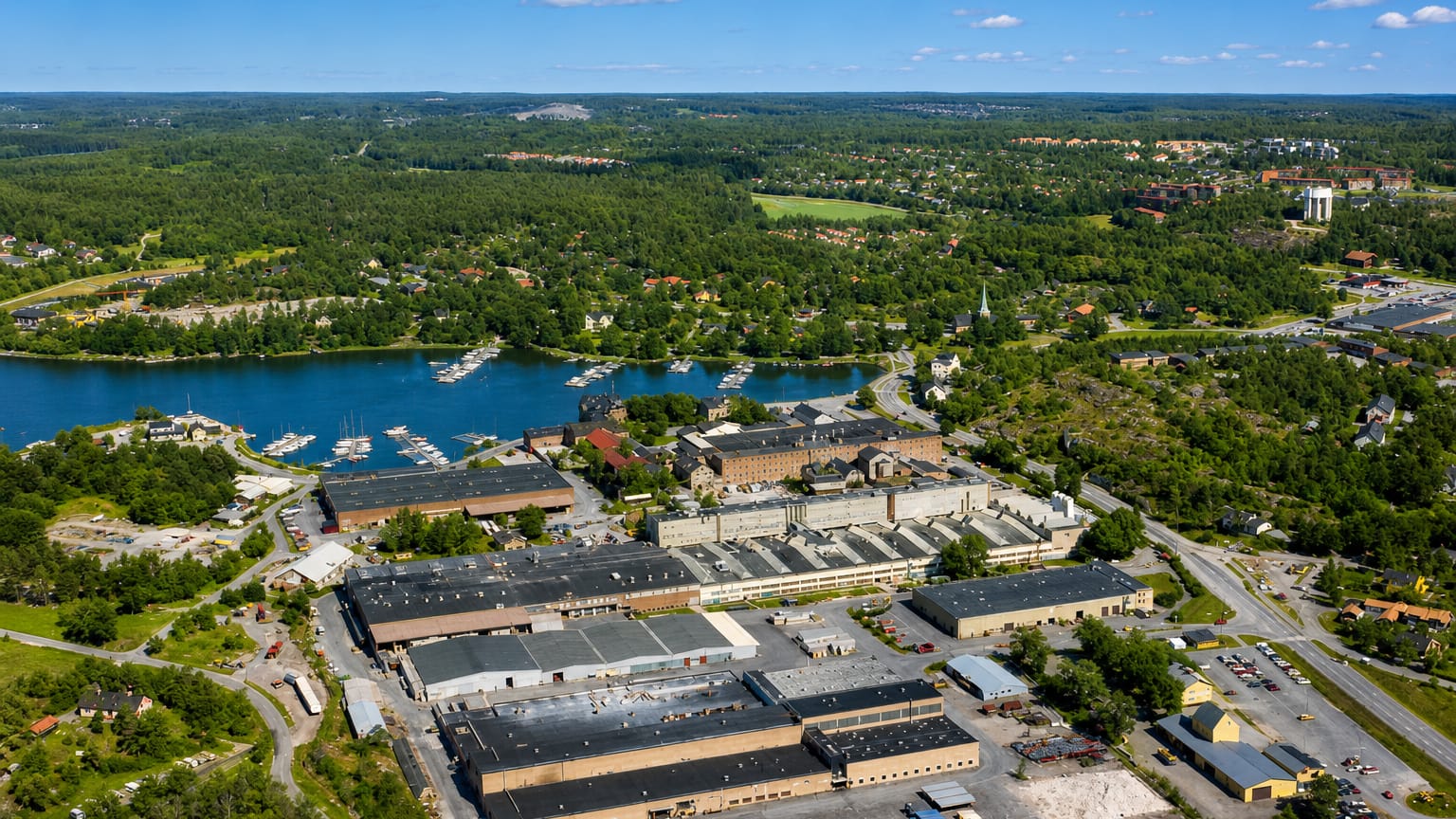 Aerial view of Gustavsberg's lakeside porcelain factory complex, marina and archipelago woodland under a blue summer sky.