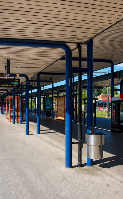Sunlit commuter-rail platform with blue pillars and a Huddinge station sign, Huddinge, Sweden