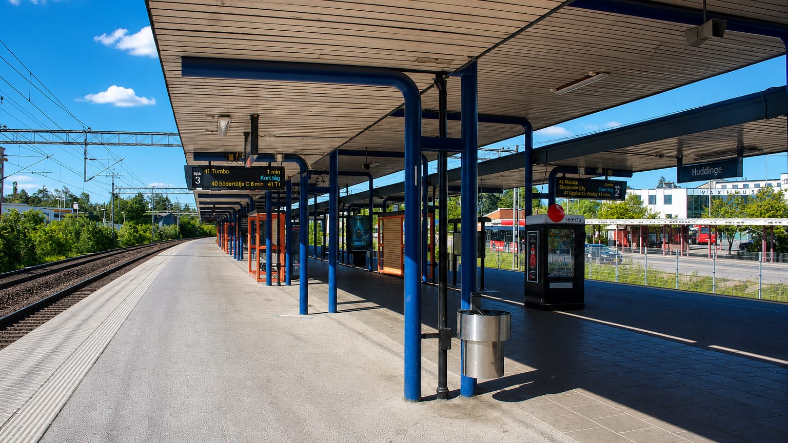 Sunlit commuter-rail platform with blue pillars and a Huddinge station sign, Huddinge, Sweden