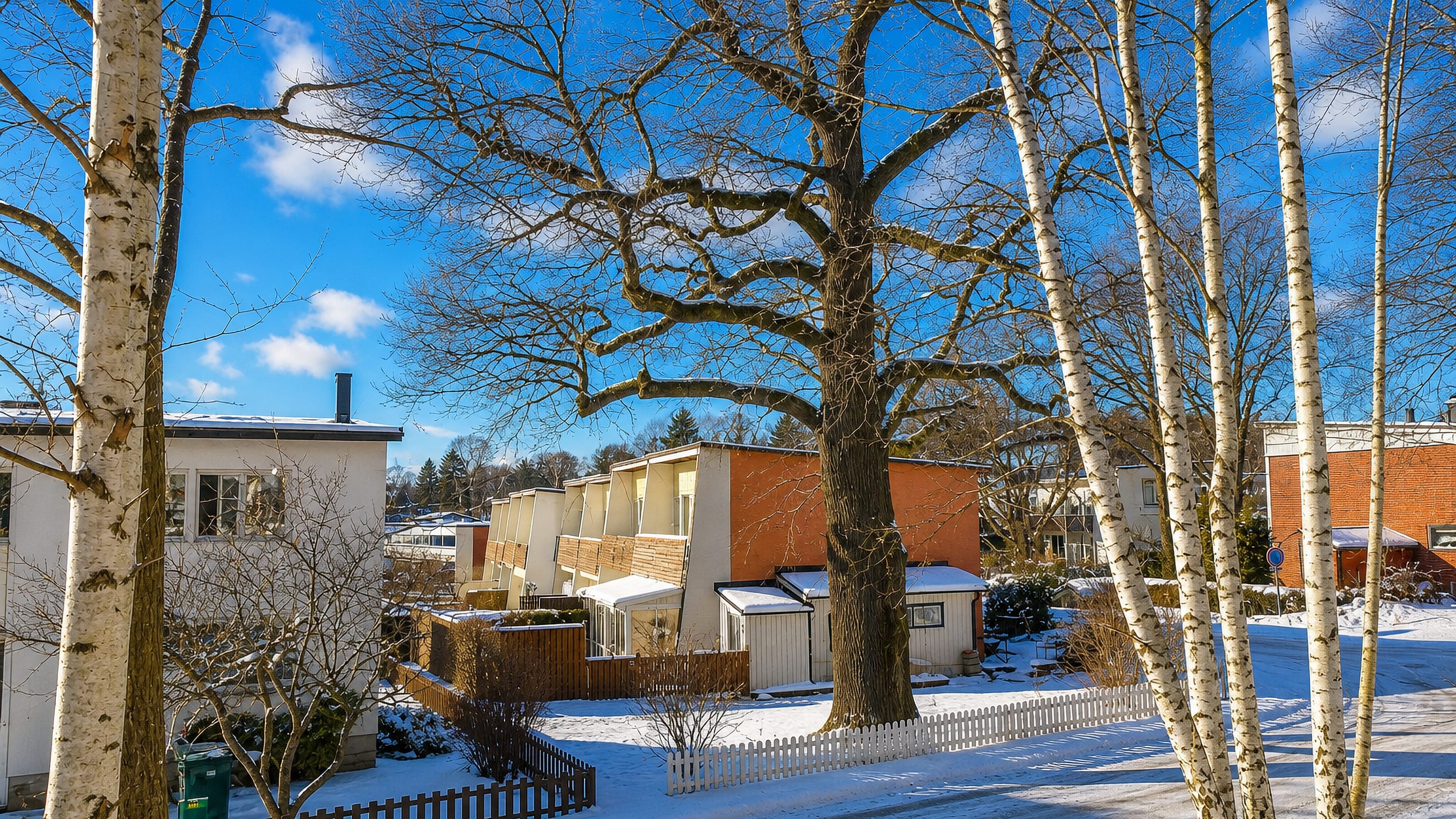 Snow-covered street of yellow and orange terraced houses among birch trees in Segeltorp, Huddinge.
