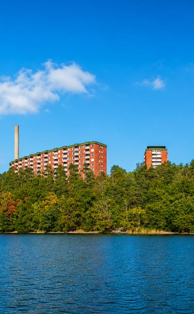 Red-brick apartment towers on a wooded Lidingö shoreline seen across the Stockholm archipelago water