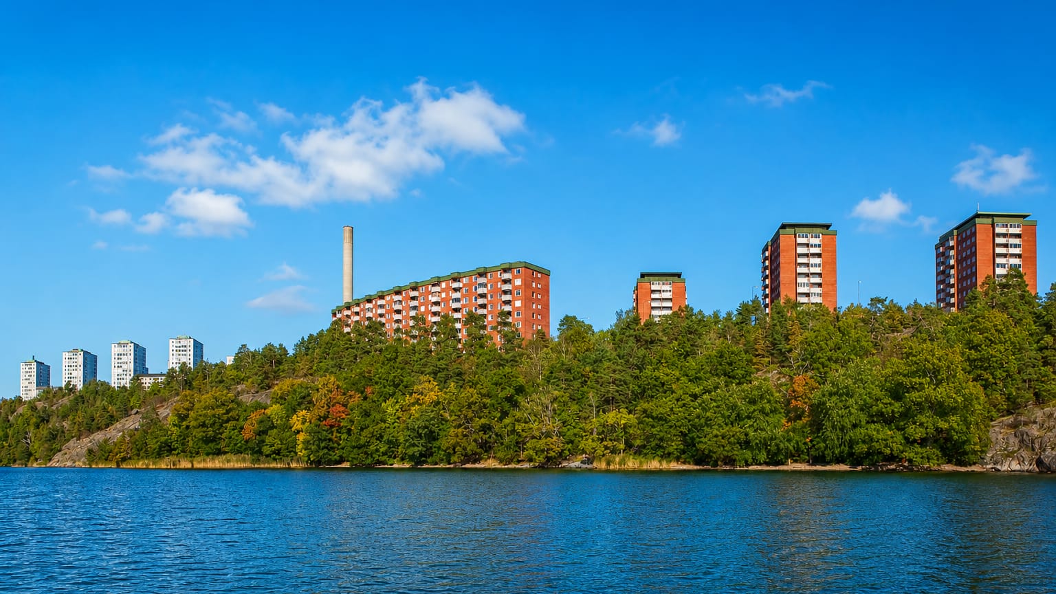 Red-brick apartment towers on a wooded Lidingö shoreline seen across the Stockholm archipelago water