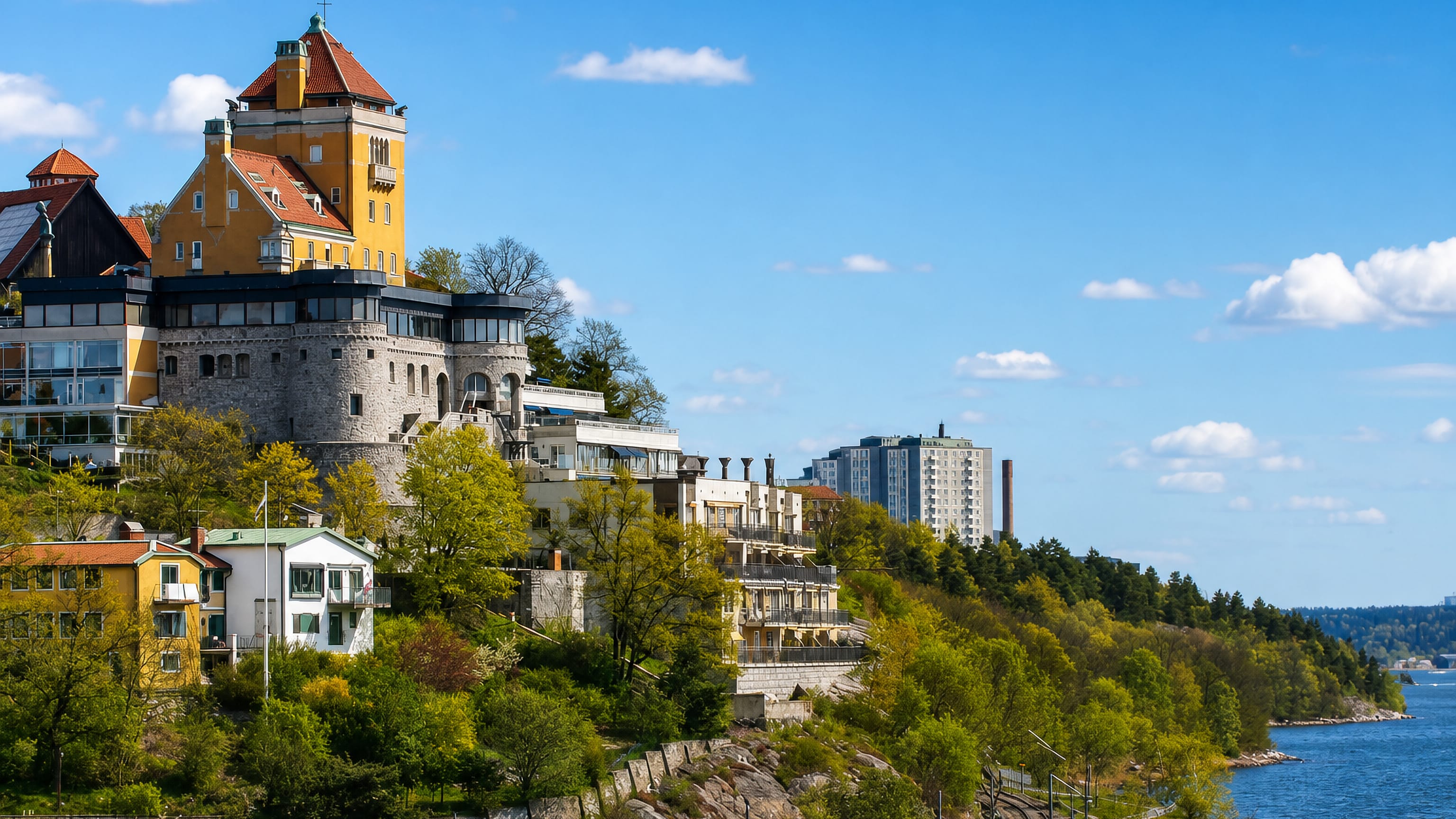 Yellow turreted villa on the wooded cliff at Herserud, Lidingo, above the blue water of Lilla Vartan.