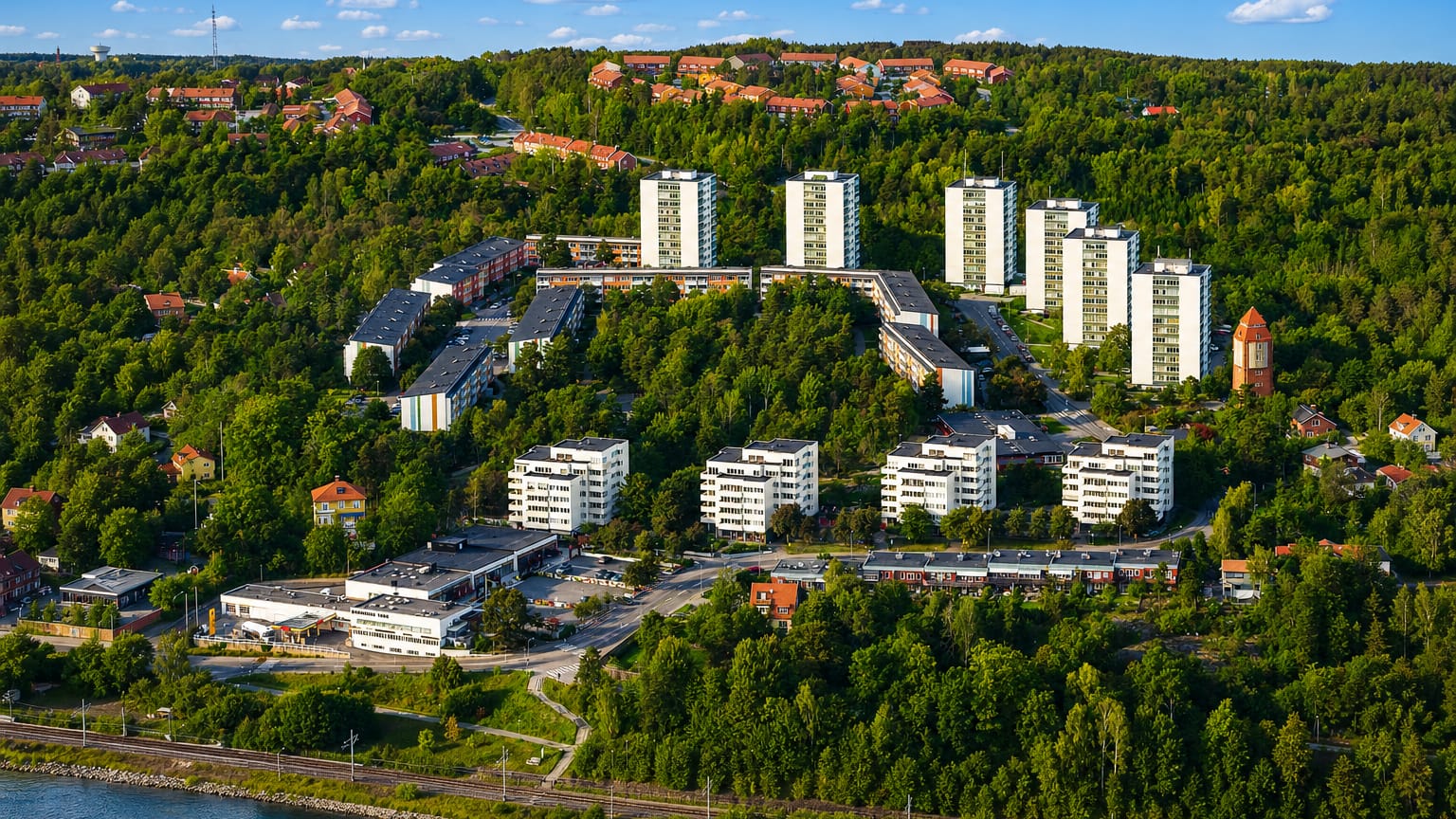 Aerial view of Skärsätra on Lidingö: apartment towers and red-roofed homes on a forested slope above a waterfront rail line