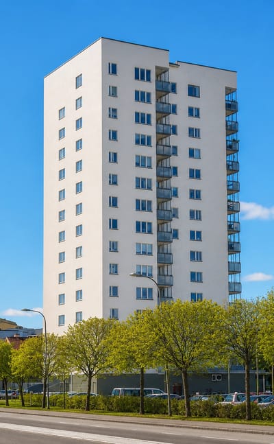 A tall white apartment tower rising above street trees and parking in Märsta, near Stockholm.