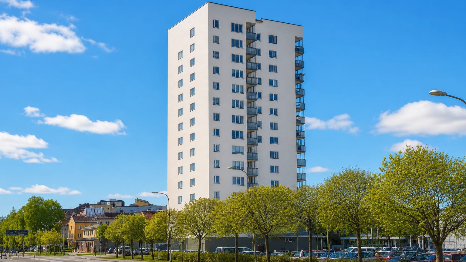 A tall white apartment tower rising above street trees and parking in Märsta, near Stockholm.