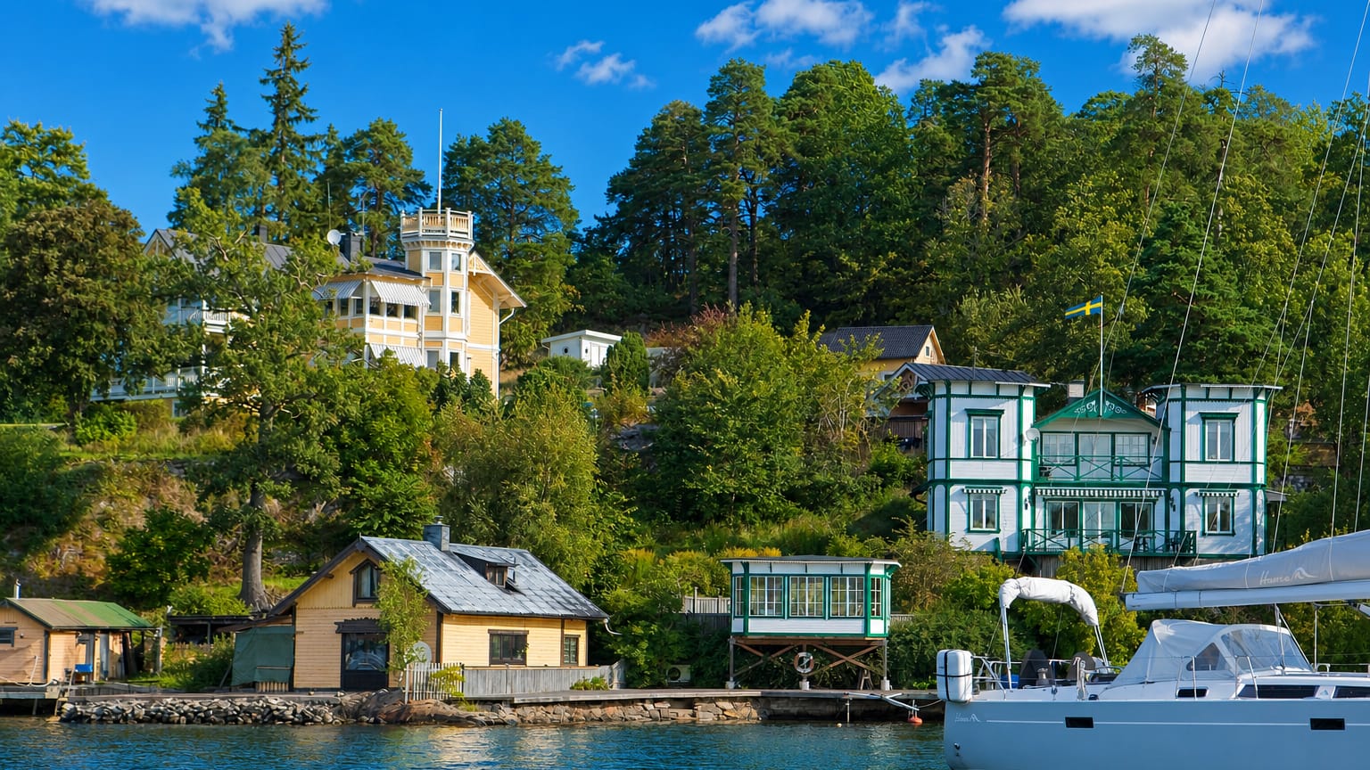 Traditional waterfront villas with a Swedish flag and a moored sailboat below a forested shore in Boo, Nacka, Sweden.