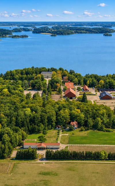 Aerial view of a lakeside manor, red farm buildings, forests and fields near Nykvarn, Sweden.