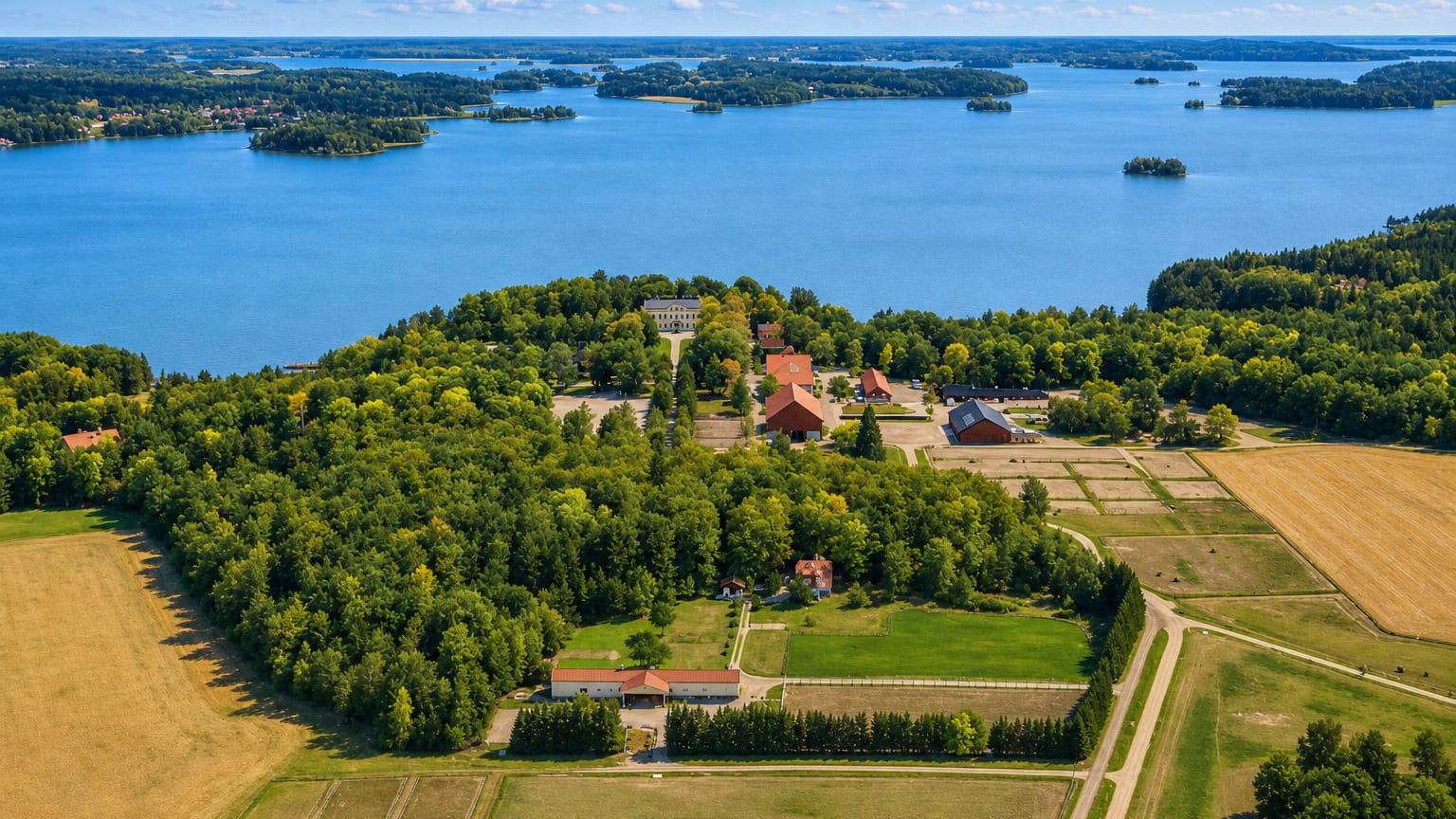 Aerial view of a lakeside manor, red farm buildings, forests and fields near Nykvarn, Sweden.