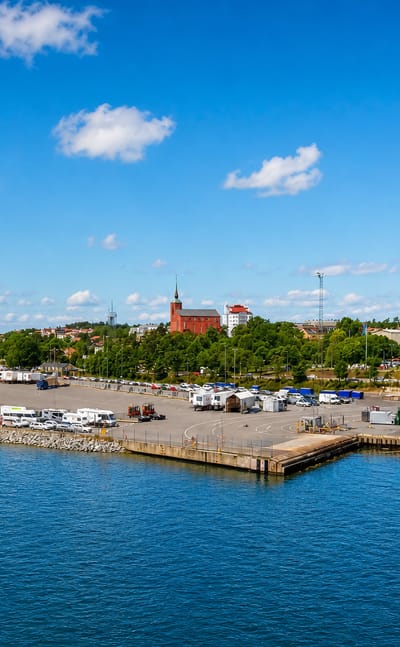 Nynäshamn, Sweden, seen from the water with its ferry port, hillside church and marina under a blue sky.