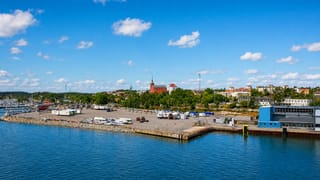 Nynäshamn, Sweden, seen from the water with its ferry port, hillside church and marina under a blue sky.
