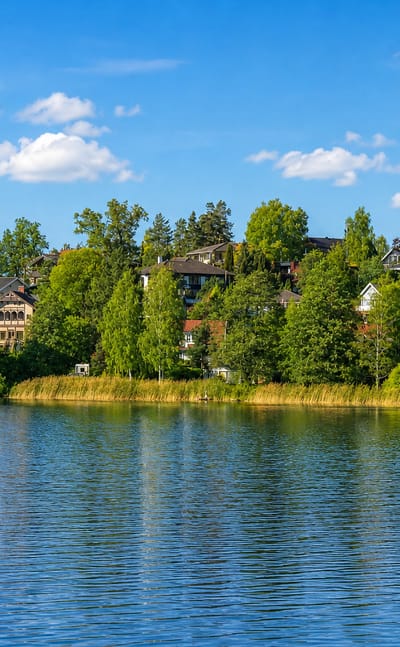 Lakeside villas set among trees reflected in calm water at Ronninge in Stockholm County, Sweden.