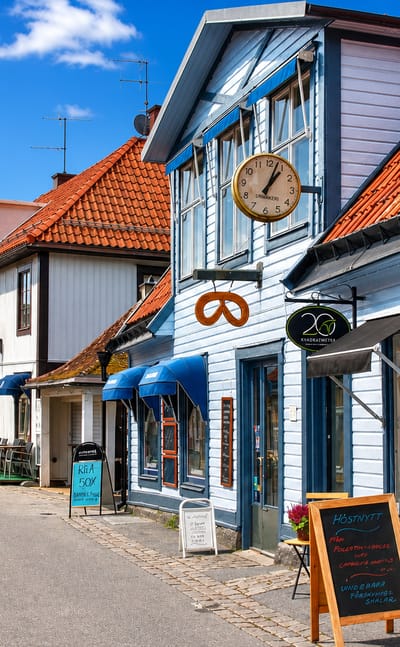 Colorful old wooden shops and houses along Sigtuna's historic cobbled main street, Stora Gatan, under a blue sky.