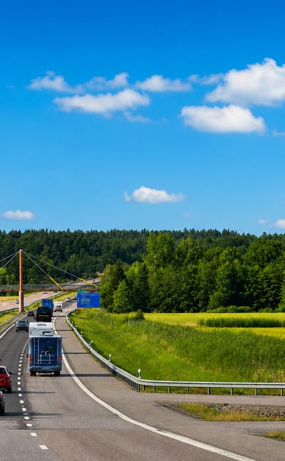 A motorway leads past farmland toward Södertälje, Sweden, with a tall orange grain silo beside green fields.