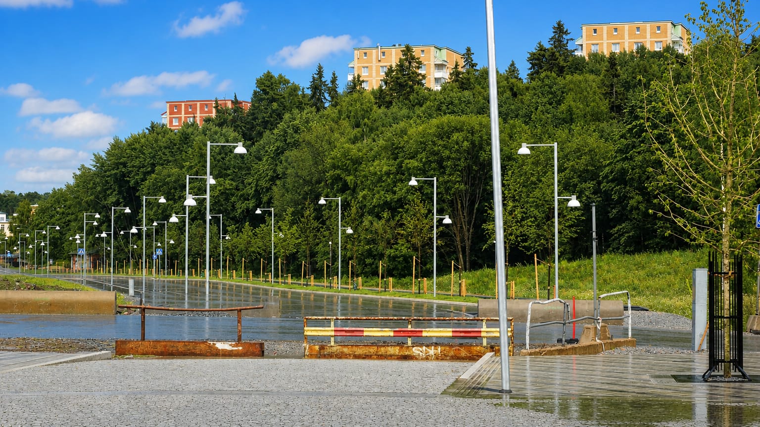 Wet paved plaza lined with street lamps in Järva, Stockholm, with modernist apartment blocks set among green wooded hills.