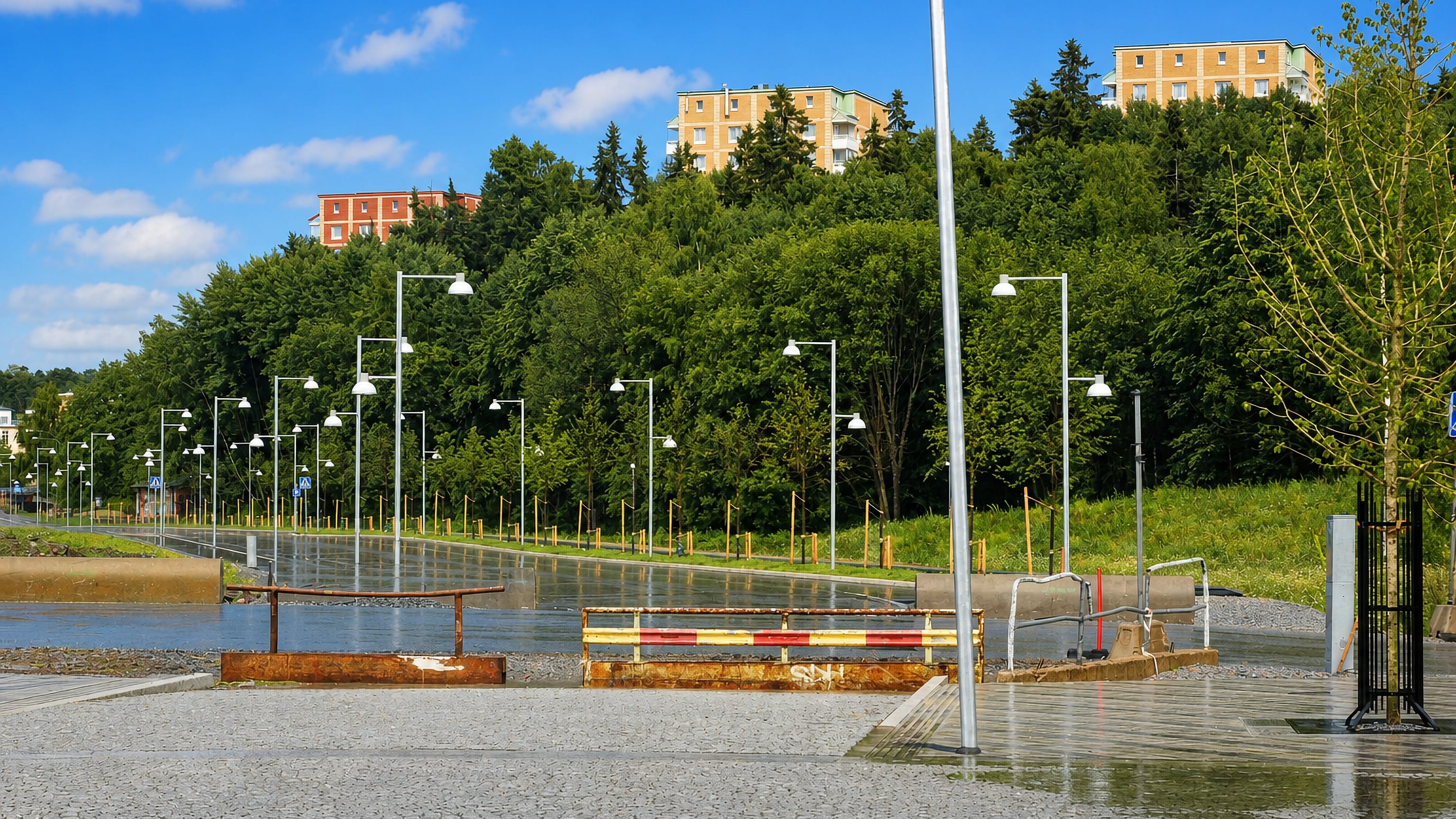 Wet paved plaza lined with street lamps in Järva, Stockholm, with modernist apartment blocks set among green wooded hills.