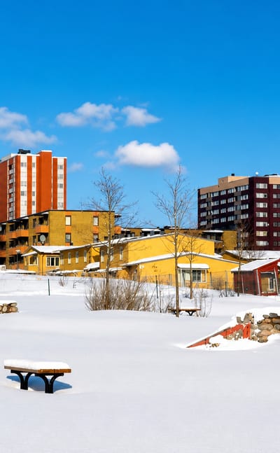 Snow-covered field in Akalla, Stockholm, bordered by red and brown high-rise apartment towers under a clear winter sky.