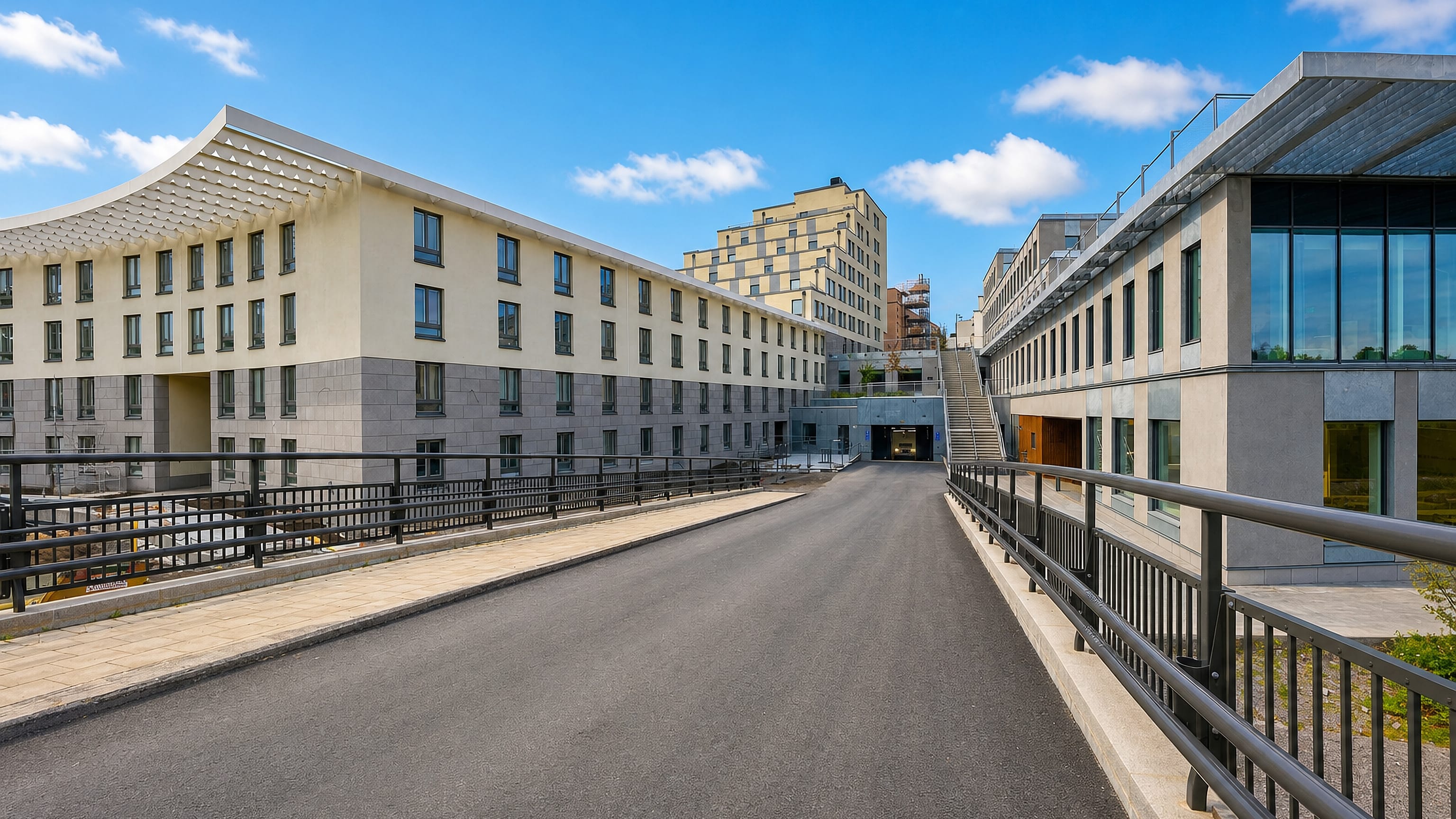 Modern pale-stone campus buildings along a quiet road in Albano, Stockholm.