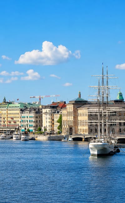 Stockholm's Gamla Stan waterfront with ochre facades, Riddarholmen spire and a moored tall ship under blue sky