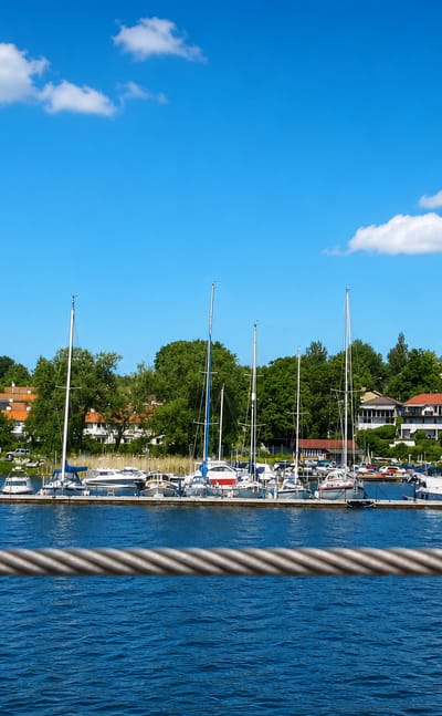Sailboat marina on Lake Mälaren backed by red-roofed villas and leafy shoreline at Hässelby Villastad, Stockholm.